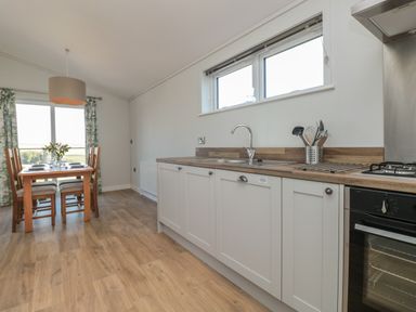 A kitchen with wooden floor a dining table with chairs and kitchen cabinets at Primrose Lodge Norton near Dartmouth