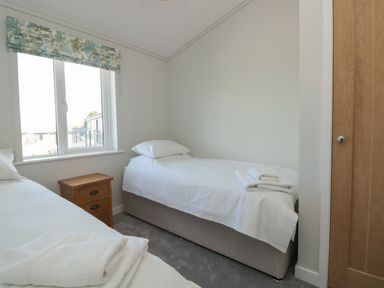 A bedroom with two single beds bedside table and window at Primrose Lodge in Norton near Dartmouth