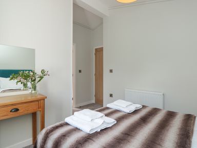 A bedroom with a bed covered by a brown and beige striped blanket and folded white towels on top next to a wooden dressing table with a vase of flowers Primrose Lodge Norton near Dartmouth
