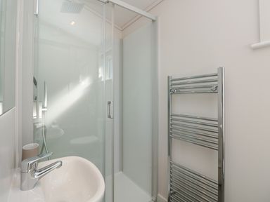 A bathroom with a sink, glass shower enclosure, and a chrome towel radiator at Primrose Lodge in Norton near Dartmouth