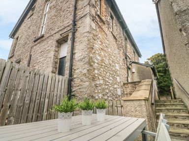 An outdoor seating area with a table and three potted plants next to a stone building and stairs at Church View in Grange-Over-Sands