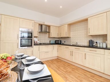 A kitchen with light wood cabinets black countertop and dining table with white plates at Church View in Grange-Over-Sands