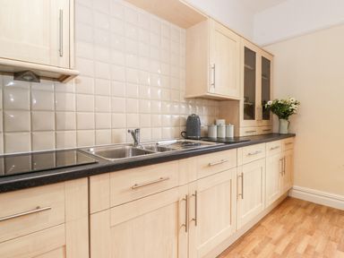 A kitchen with light wood cabinets a black countertop a double sink a kettle canisters and flowers at Church View in Grange-Over-Sands