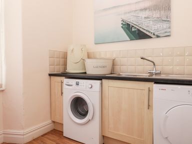 A laundry room with washing machine, sink, laundry basket, and wall art at Church View in Grange-Over-Sands