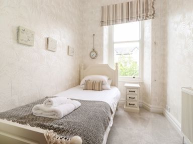 A bedroom with a single bed, bedside table, window with striped blind, and wall decorations at Church View in Grange-Over-Sands