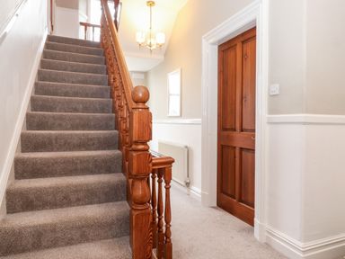 A carpeted staircase with a wooden banister and a wooden door in a hallway at Church View in Grange-Over-Sands