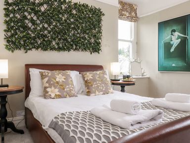 A bedroom with a bed with floral pillows and rolled towels on it at Church View in Grange-Over-Sands