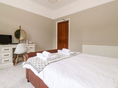 A bedroom with a bed with white linens and rolled towels a white desk with a chair and a round mirror at Church View in Grange-Over-Sands