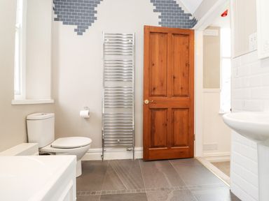 A bathroom with a toilet a towel radiator a wooden door and a sink at Church View in Grange-Over-Sands