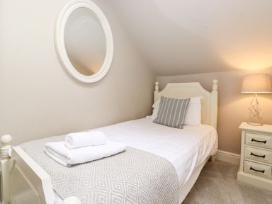 A single bed with striped pillow and folded towels next to a nightstand with lamp in a bedroom at Church View in Grange-Over-Sands