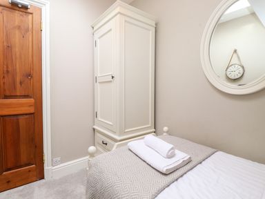 A bedroom corner with a wooden door a white wardrobe a bed with folded towels and a round mirror on the wall at Church View in Grange-Over-Sands