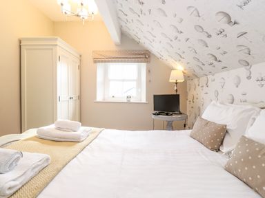 A bedroom with a double bed with polka dot pillows a wardrobe window with a blind and a side table with a lamp and television at Church View in Grange-Over-Sands
