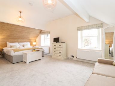 A bedroom with a large bed a chest of drawers with a TV a window a full-length mirror and a sofa at Church View in Grange-Over-Sands