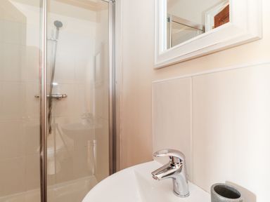 A bathroom with a shower enclosure a sink with a faucet and a mirror above at Church View in Grange-Over-Sands