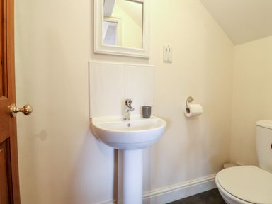 A bathroom with a pedestal sink mirror toilet and toilet paper holder at Church View in Grange-Over-Sands