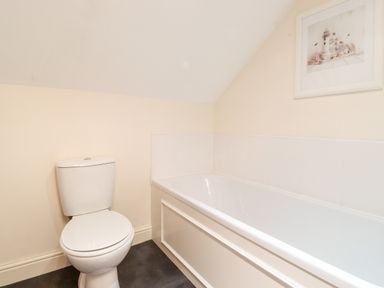 A bathroom with a toilet and a bathtub with a framed picture on the wall at Church View in Grange-Over-Sands