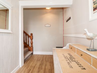 An entryway with wooden stairs on the left a bench with storage drawers and a bird sculpture on the right and a mirror on the left wall at Church View in Grange-Over-Sands
