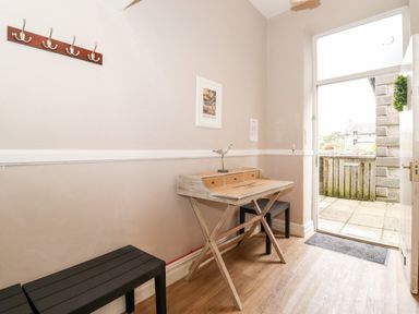An entryway with a wooden desk and two black benches near an open door at Church View in Grange-Over-Sands