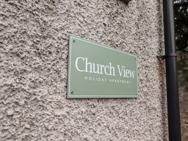 A green sign on a textured wall that reads Church View Holiday Apartment at Church View in Grange-Over-Sands