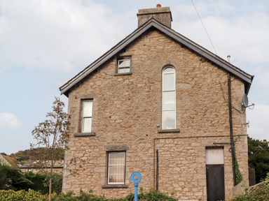 A stone building with windows and a chimney with a blue circular sign in front at Church View in Grange-Over-Sands