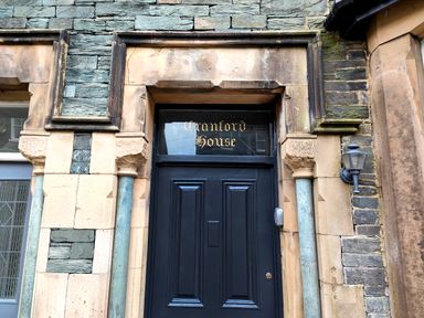 Black door with gold lettering Cranford House above in a stone building with decorative pillars and a wall lantern at Cranford House Keswick