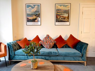 A blue sofa with orange and multicolored cushions in a living room with a wooden coffee table holding a potted plant at Cranford House in Keswick