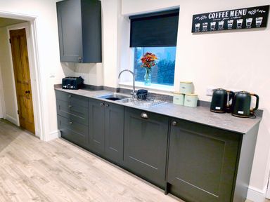 A kitchen with dark cabinets a sink toaster kettle and coffee canisters at Cranford House in Keswick