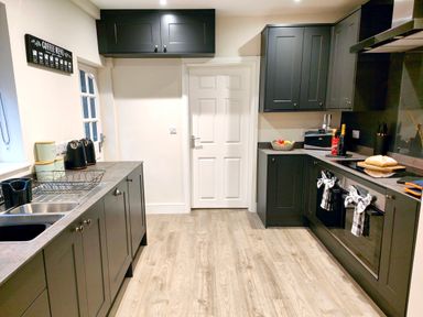 A kitchen with dark cabinets, countertop appliances, a sink, oven, and a door at Cranford House in Keswick