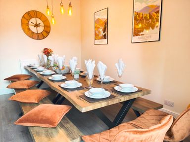 A dining room with a long wooden table set with plates glasses and napkins surrounded by benches and chairs with cushions at Cranford House in Keswick