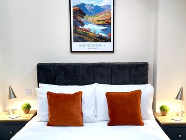 A bedroom with a bed with orange cushions and white pillows and bedside tables with lamps at Cranford House in Keswick