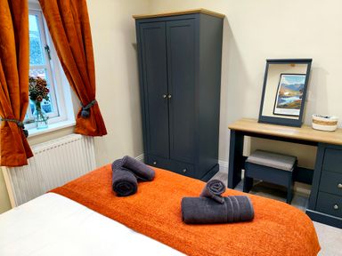 A bedroom with an orange bed cover gray wardrobe dressing table and orange curtains at Cranford House in Keswick