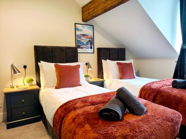 A bedroom with two single beds with red throws and pillows side tables with lamps and small plants at Cranford House in Keswick