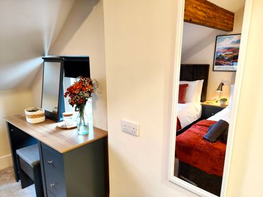 A dressing table with a mirror flowers and basket beside a wall mirror reflecting a bedroom with two beds at Cranford House in Keswick