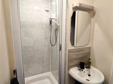 A bathroom with a shower enclosure a sink a mirror and a soap dispenser at Cranford House in Keswick