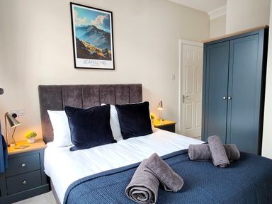 A bedroom with a bed with pillows and rolled towels bedside tables with lamps and a blue wardrobe at Cranford House in Keswick
