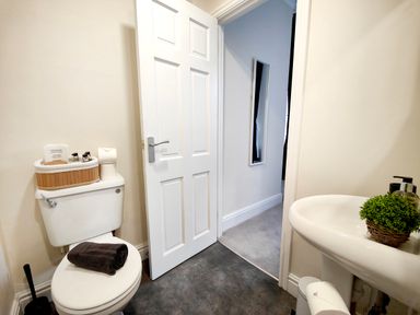 A bathroom with a toilet, sink, and open door showing a hallway at Cranford House Keswick