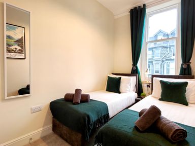A bedroom with two single beds green pillows and blankets and a window with green curtains at Cranford House in Keswick