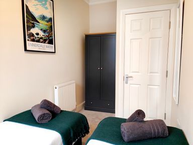 A bedroom with two single beds with green blankets and rolled towels a black wardrobe white door and a framed picture on the wall at Cranford House in Keswick