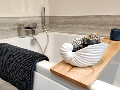 A bathtub with a dark towel hanging on the side a wooden bath tray with a white decorative shell and pot at Cranford House in Keswick