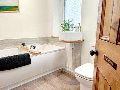 A bathroom with a bathtub a sink a toilet and a wooden door at Cranford House in Keswick