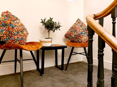 Two chairs with colorful cushions and a small table with a potted plant between them near a staircase