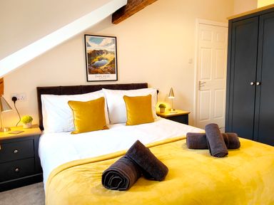 A bedroom with a double bed with yellow cushions and blankets and rolled towels on it at Cranford House in Keswick