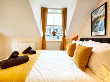 A bedroom with a bed with yellow pillows and rolled towels near a window with yellow curtains and a framed picture on the wall at Cranford House in Keswick