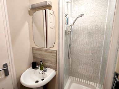 A bathroom with a sink soap dispenser mirror and a shower with a glass door at Cranford House in Keswick