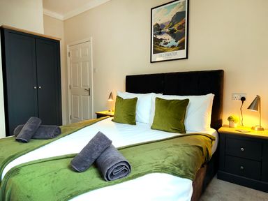 A bedroom with a bed featuring green throws and pillows bedside tables lamps a wardrobe and a door at Cranford House Keswick