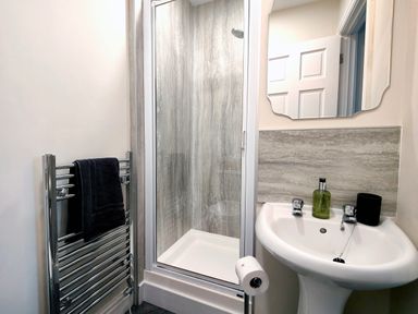 A bathroom with a shower enclosure a pedestal sink a mirror a towel radiator with a black towel and a roll of toilet paper at Cranford House in Keswick
