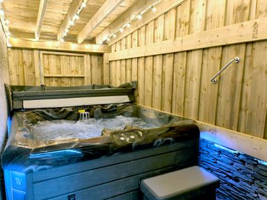 An indoor hot tub with bubbling water under string lights in a wooden room at Cranford House in Keswick