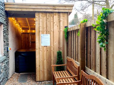 A wooden hot tub enclosure with string lights and wooden benches along a fence with hanging plants at Cranford House in Keswick