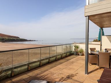 A patio with outdoor dining furniture and potted plants overlooking a beach and sea at 4 Burgh Island Causeway in Bigbury