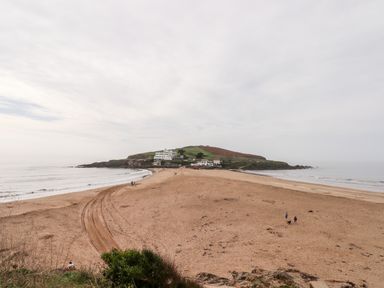 A sandy beach leading to a small island with buildings and grassy hills at 4 Burgh Island Causeway in Bigbury